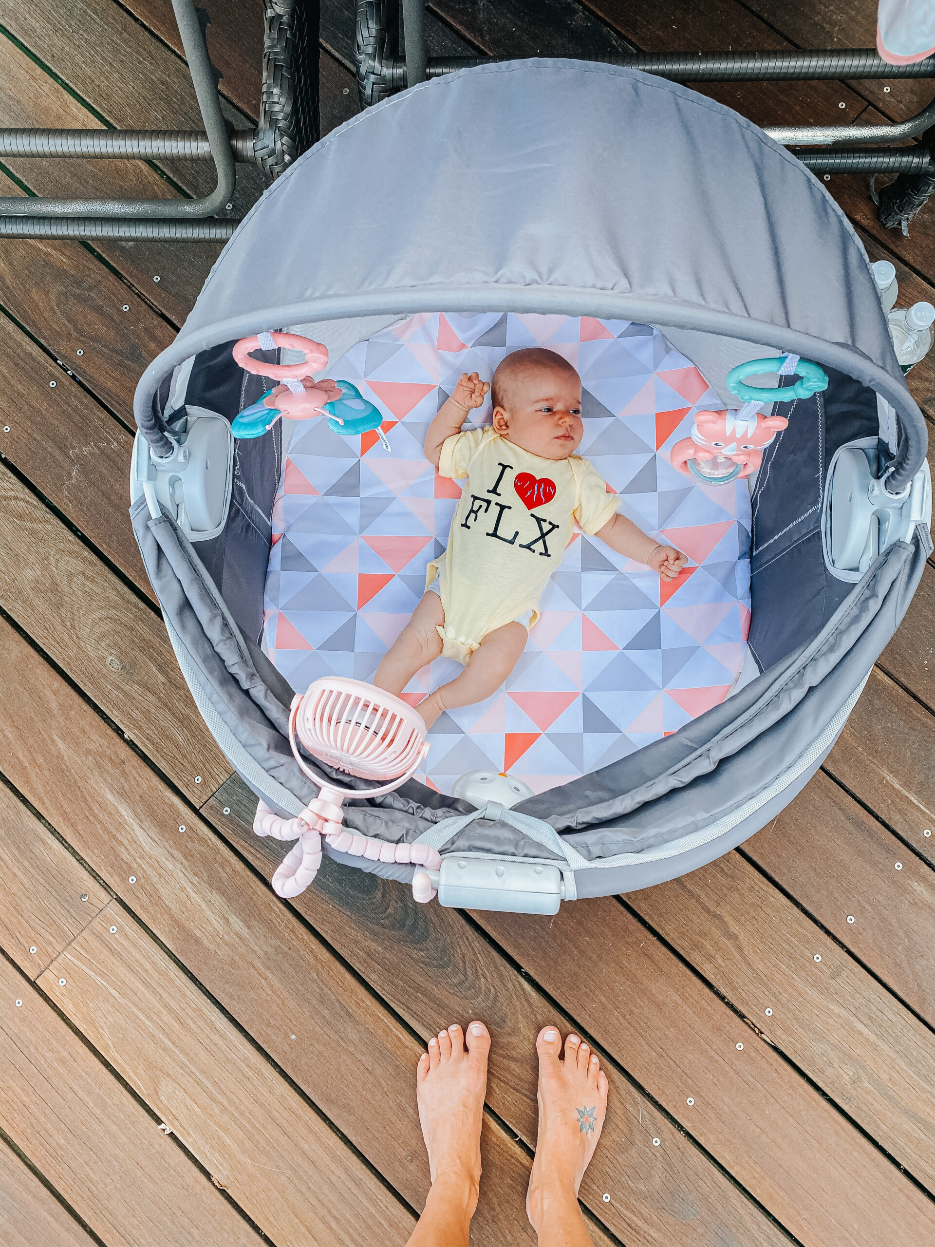 Newborn baby laying in portable dome with fan on deck in summer
